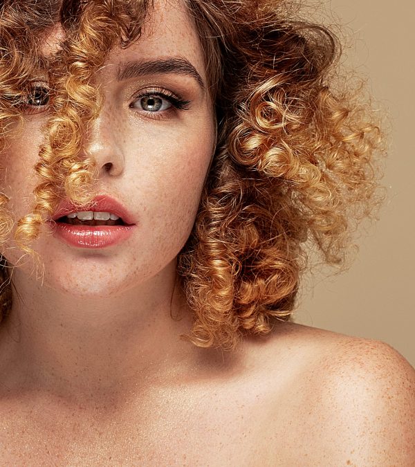 Portrait of beautiful woman with curly hairstyle and natural freckles. Redhair lady. Girl looking at camera. Studio shot.